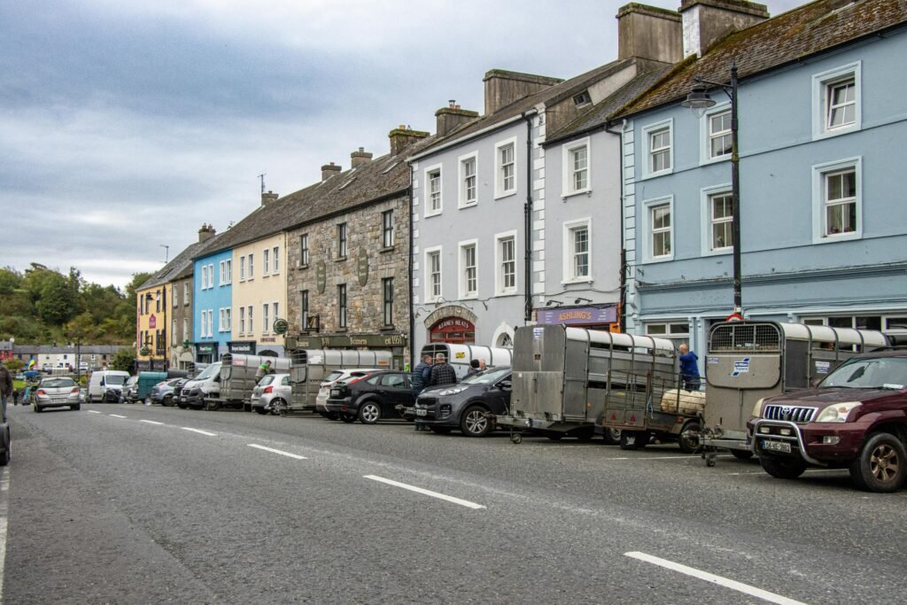 pexels-photo-28871173-28871173 Street view of Kilkelly, Ireland showcasing colorful buildings and parked farming trailers along the road.