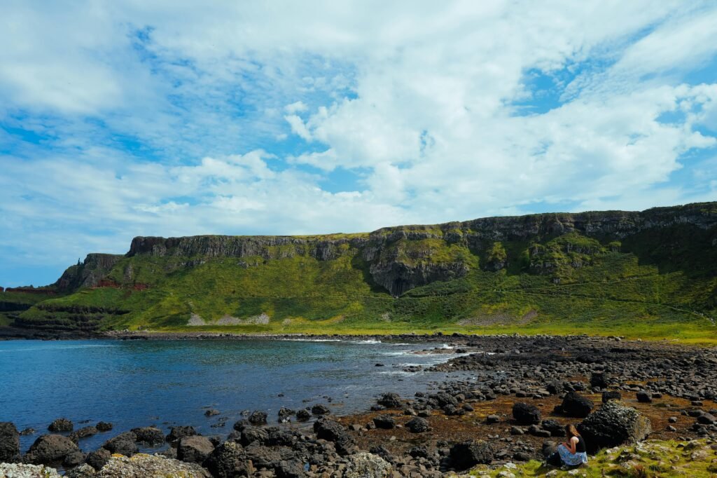 Breathtaking coastal landscape featuring lush green cliffs and a rocky shoreline under a bright blue sky.