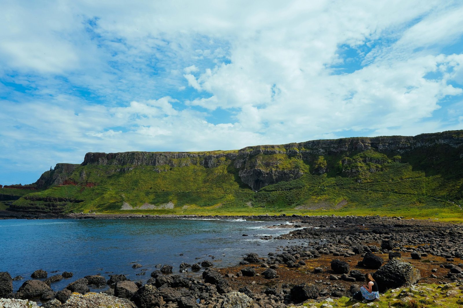 Breathtaking coastal landscape featuring lush green cliffs and a rocky shoreline under a bright blue sky.
