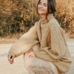 Young woman smiling outdoors in Minsk wearing a cozy beige sweater.